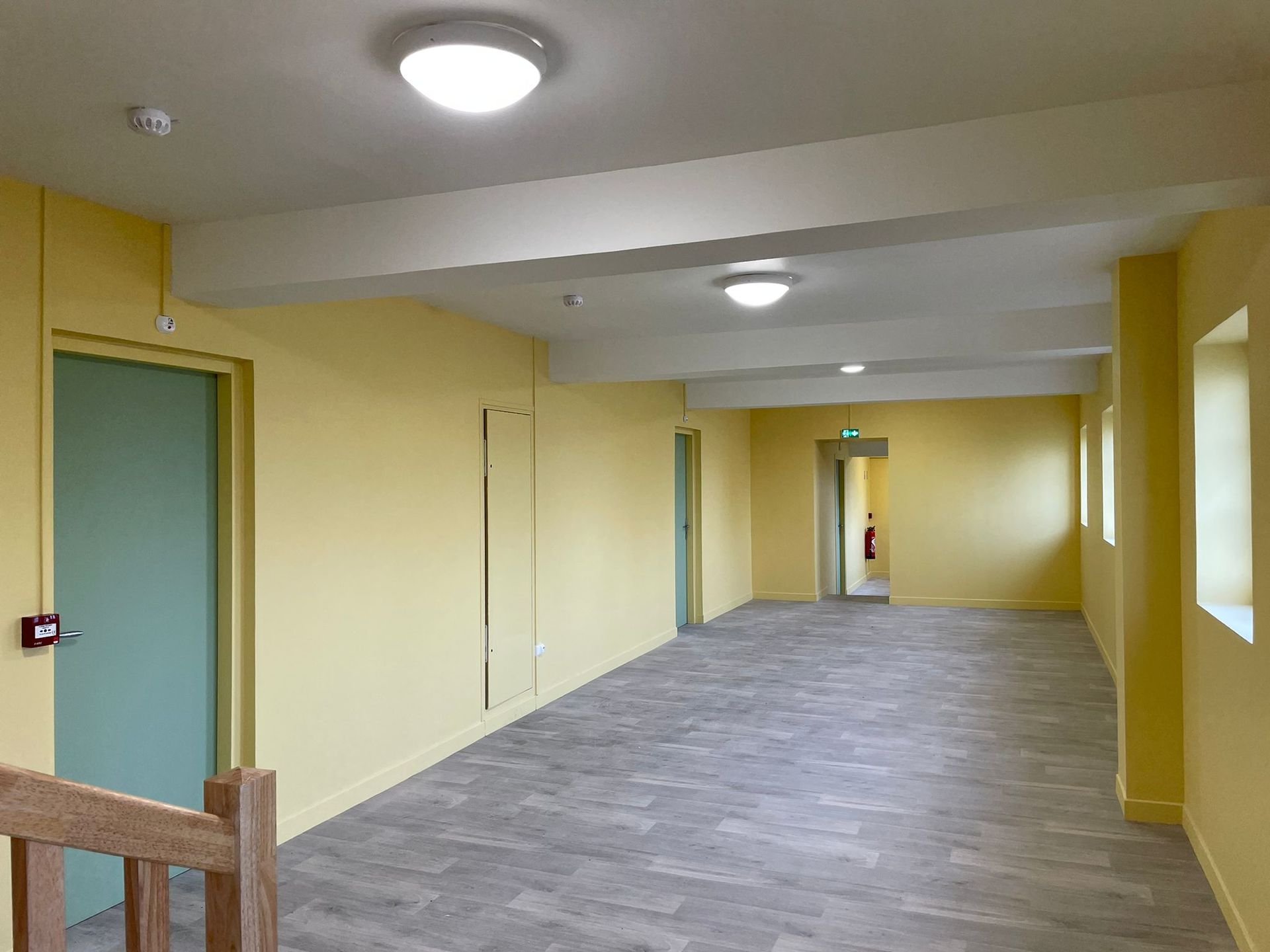 Un long couloir avec des murs jaunes et une porte verte avec notre entreprise de peinture normandie