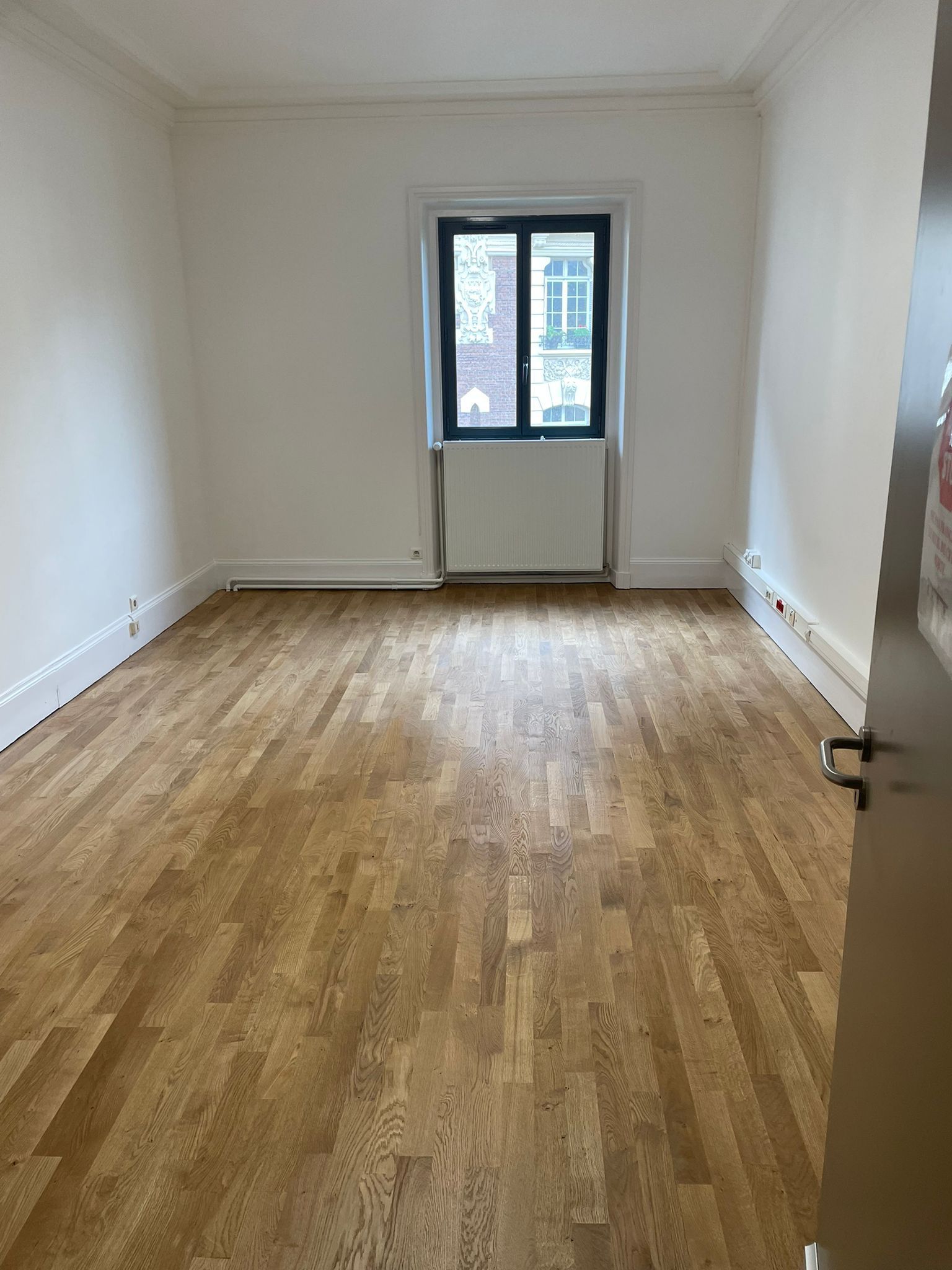 Une pièce vide avec du parquet et une fenêtre avec notre entreprise de peinture normandie.