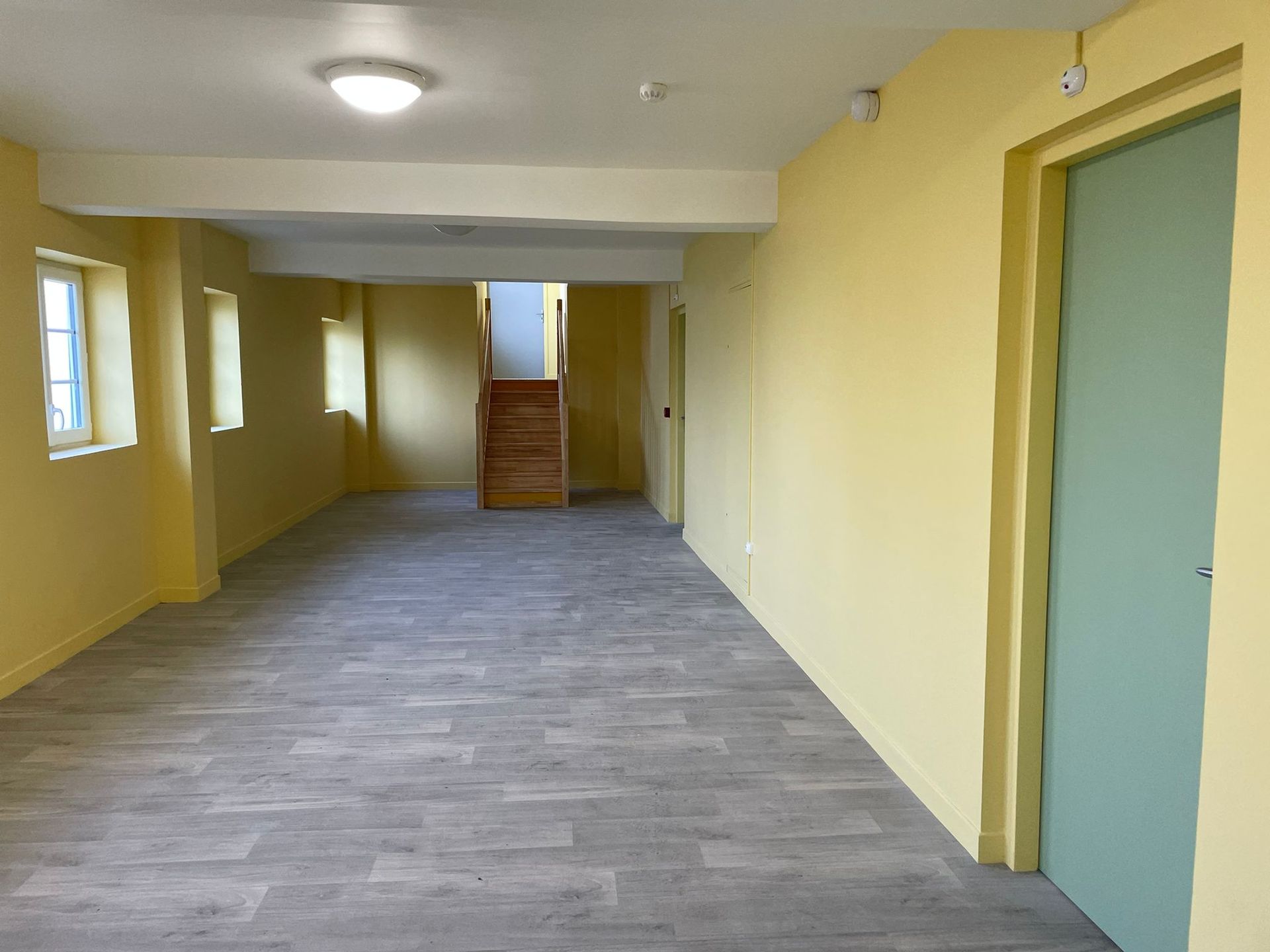 Une pièce vide avec des murs jaunes et une porte verte avec notre entreprise de peinture normandie