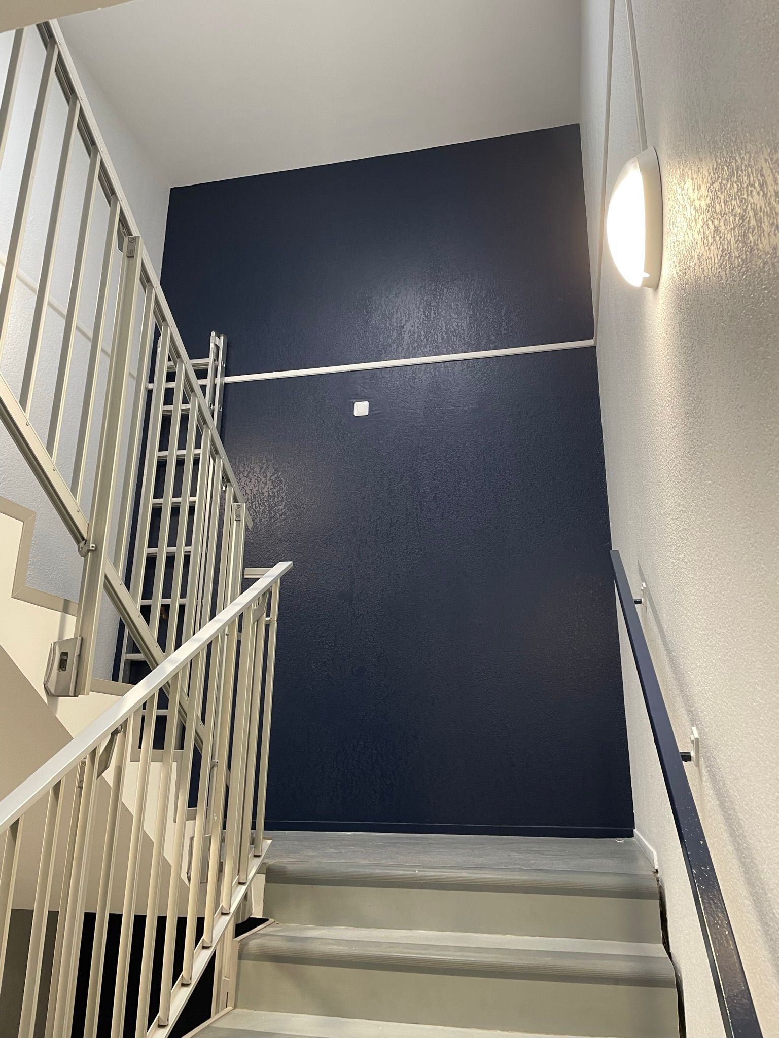 Un escalier avec un mur bleu et une rampe blanche avec notre entreprise de peinture normandie