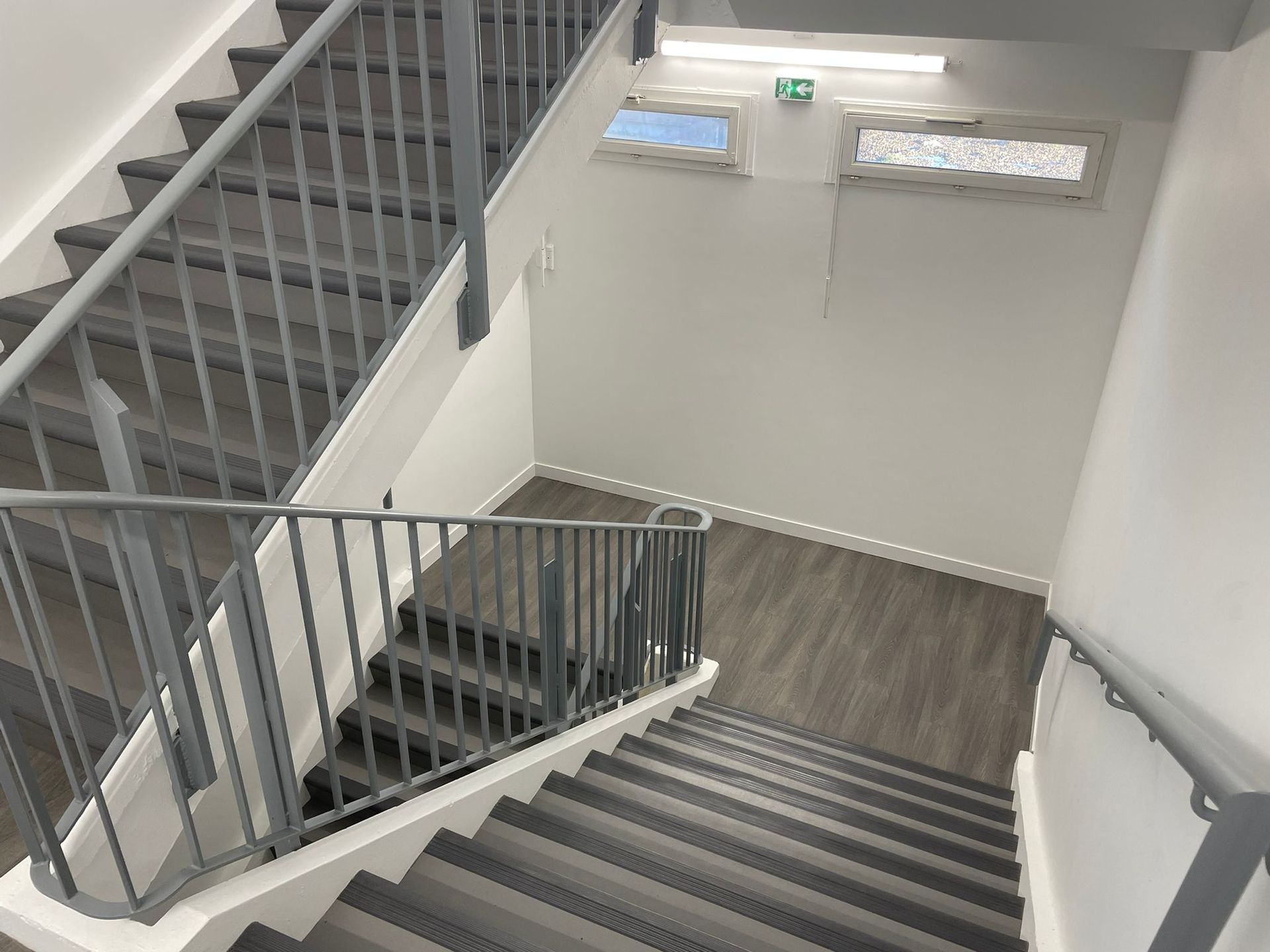 Un escalier avec une rampe en métal et un plancher en bois dans un bâtiment avec notre entreprise de peinture normandie.