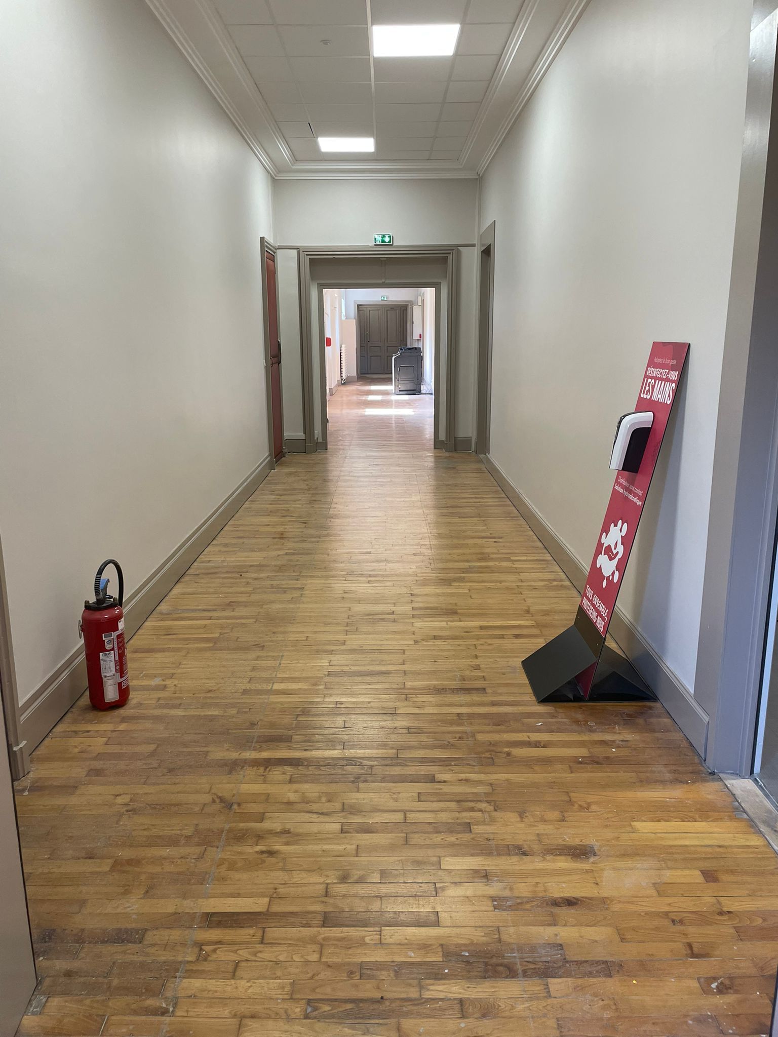 Un long couloir avec du parquet et des murs blancs avec notre entreprise de peinture normandie.