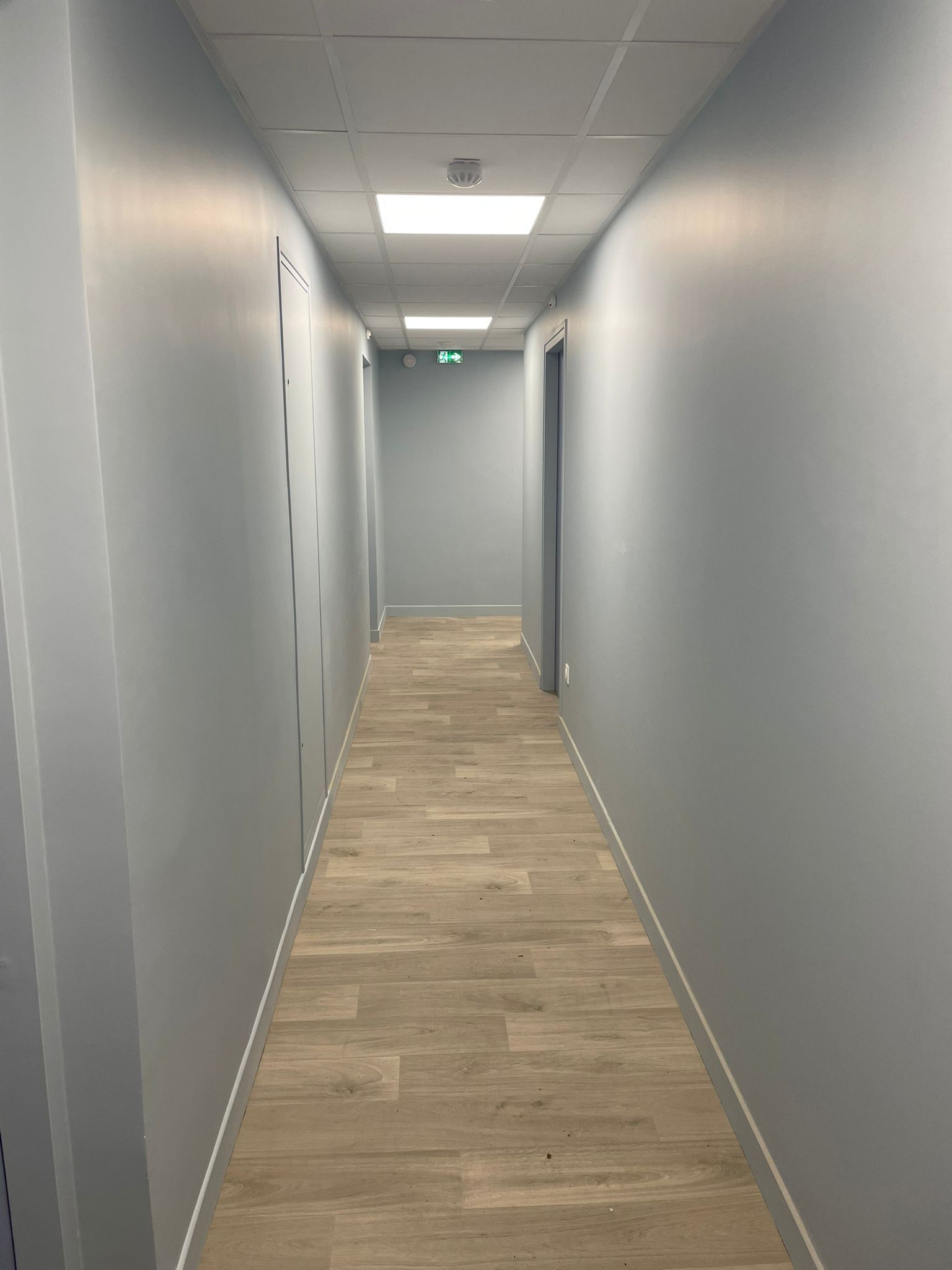 Un long couloir avec un plancher en bois et des murs gris avec notre entreprise de peinture normandie.