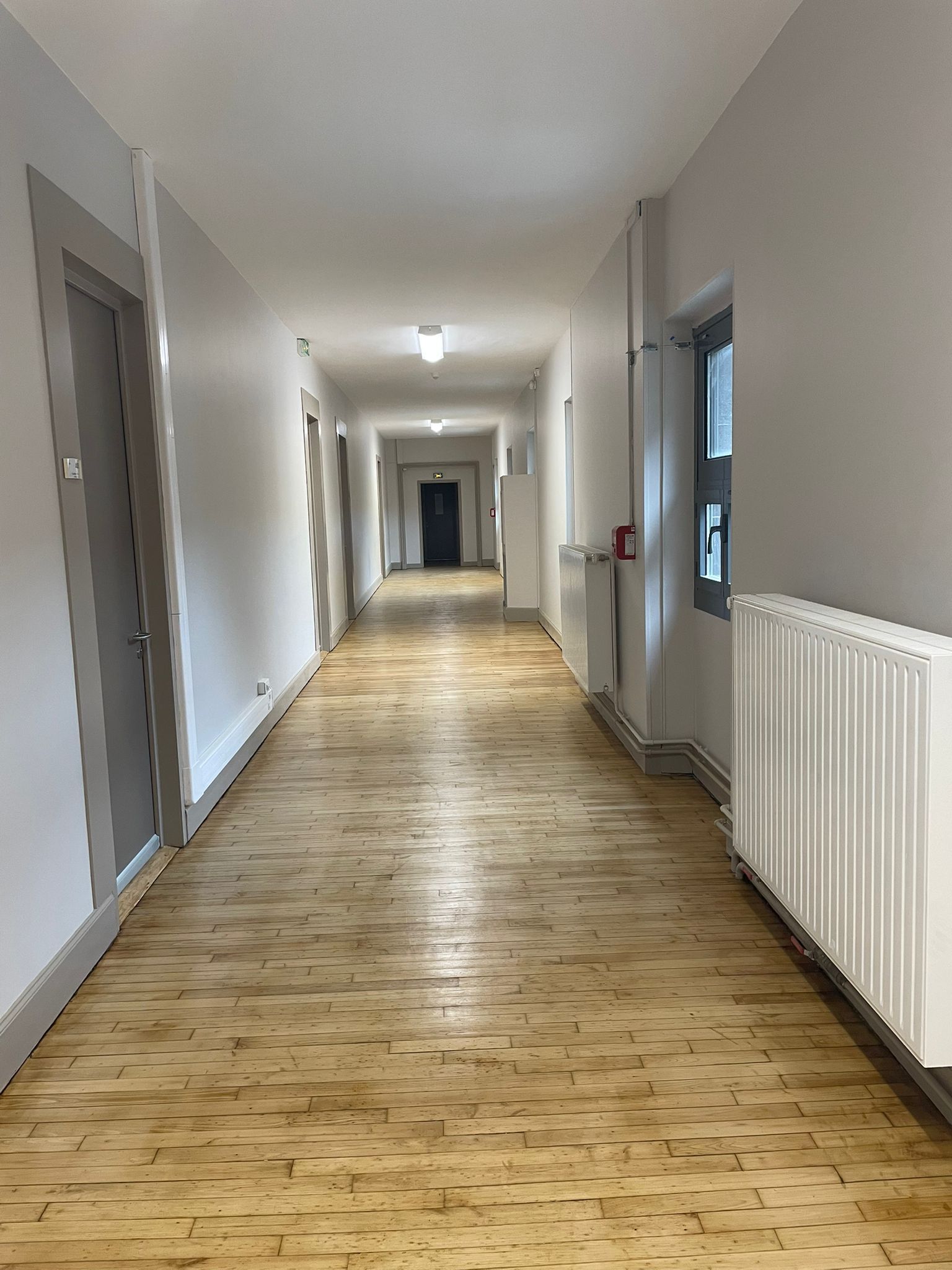 Un long couloir avec parquet et radiateurs blancs avec notre entreprise de peinture normandie.