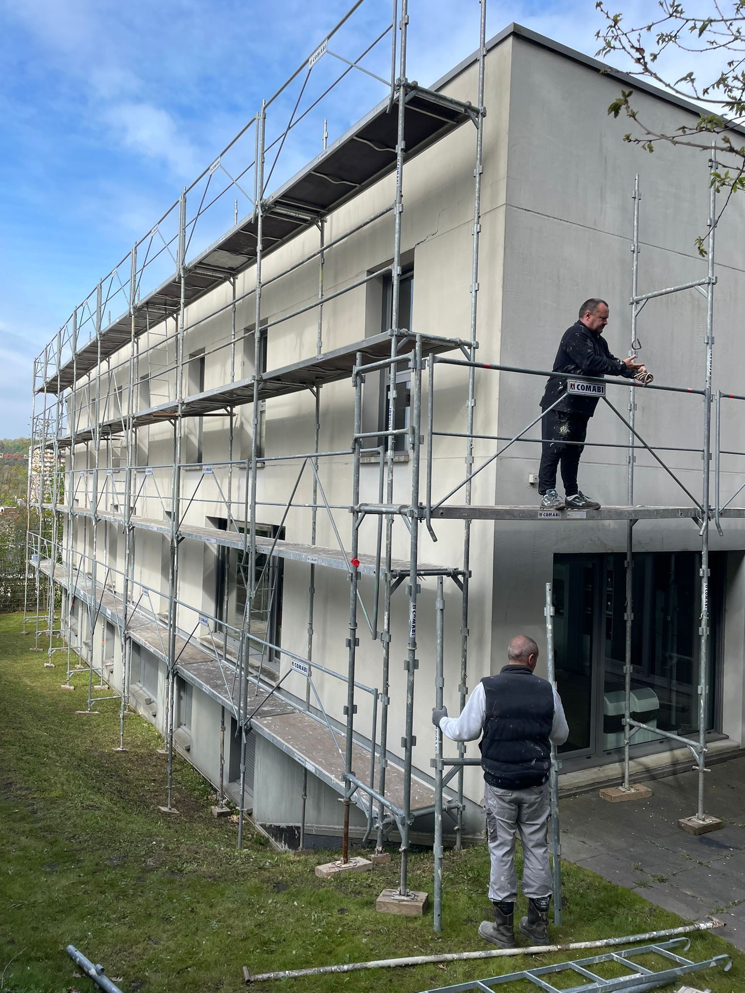 Un homme se tient debout sur un échafaudage sur le côté d'un bâtiment avec notre entreprise de peinture normandie.