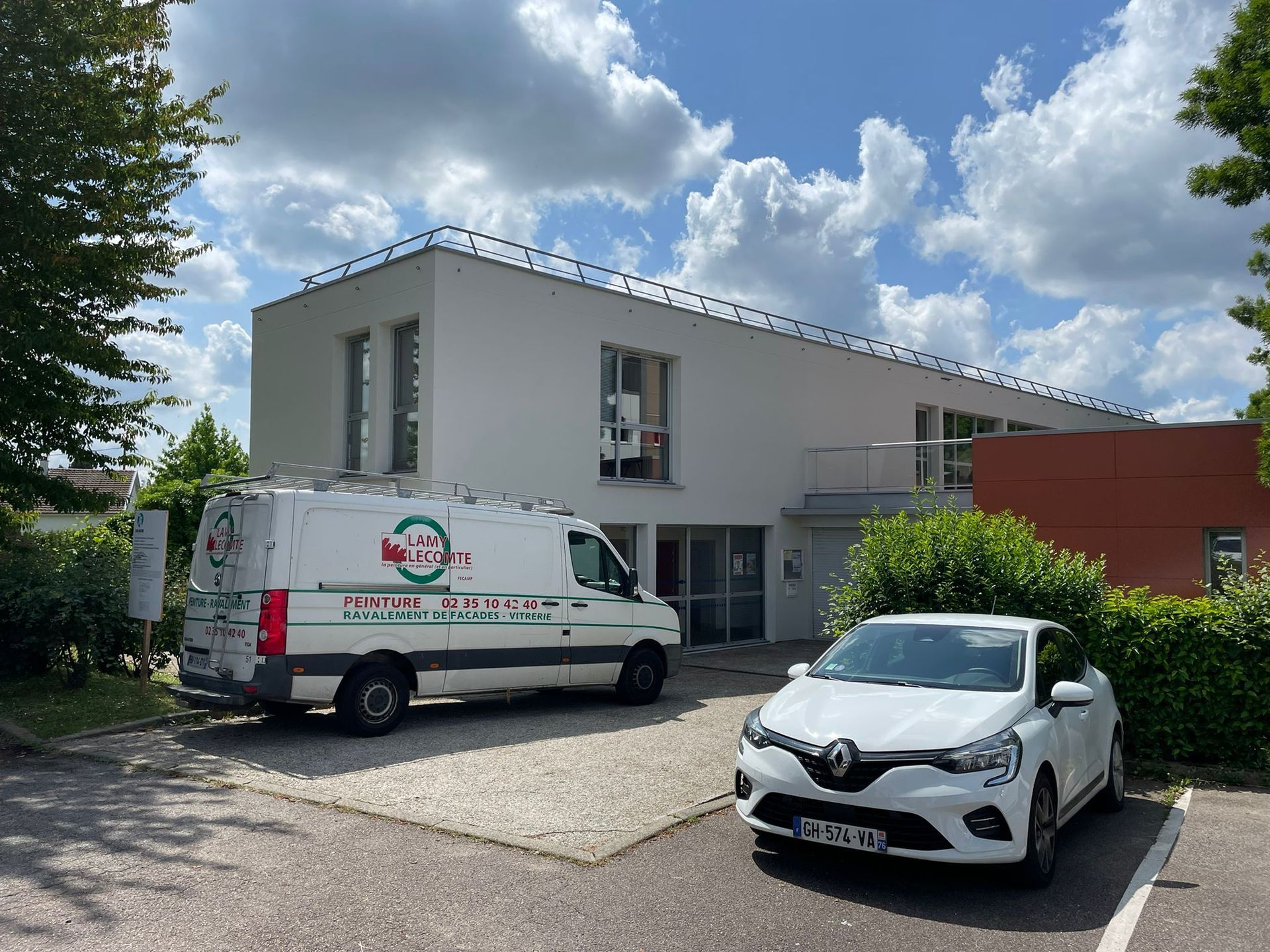 Une camionnette blanche et une voiture blanche sont garées devant un bâtiment avec notre entreprise de peinture normandie.