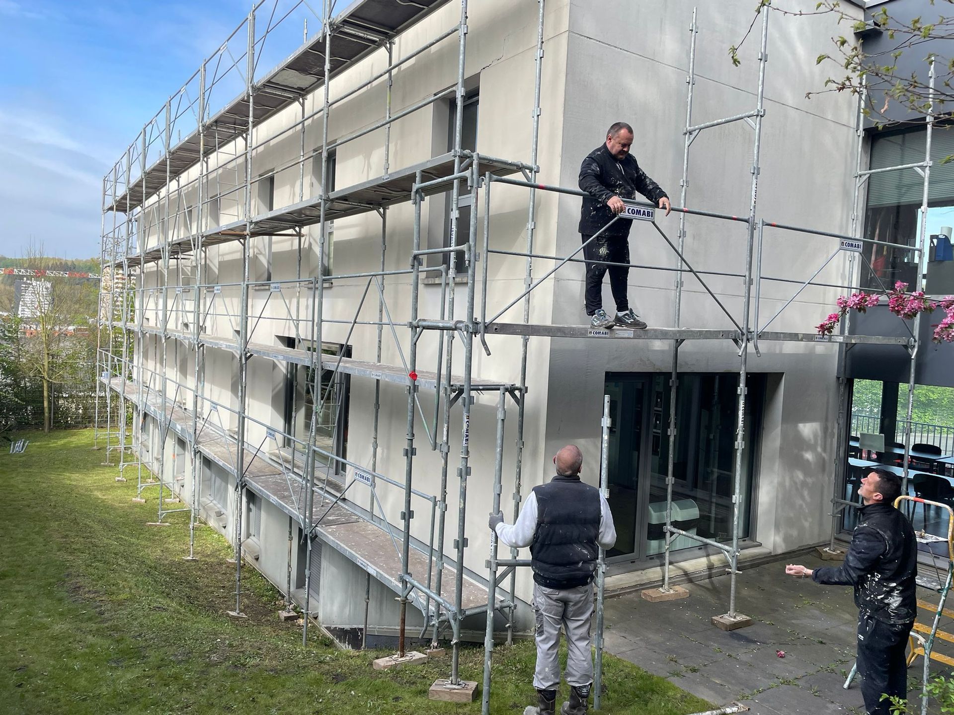 Un homme se tient debout sur un échafaudage sur le côté d'un bâtiment avec notre entreprise de peinture normandie.
