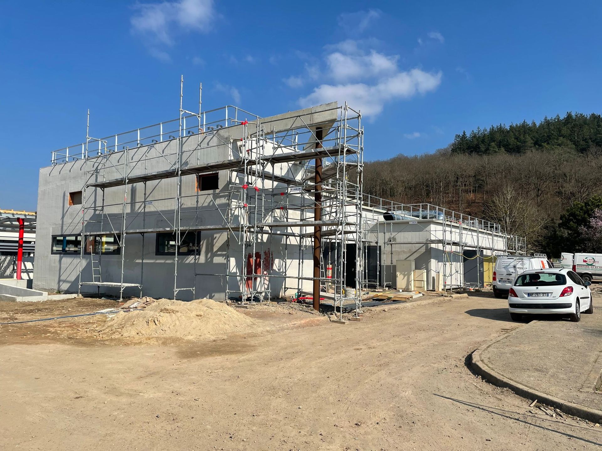 Une voiture blanche est garée devant un immeuble en construction avec notre entreprise de peinture normandie.
