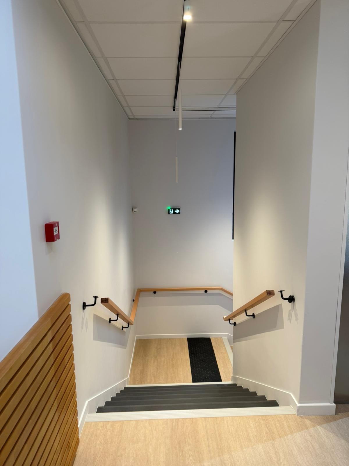 Un couloir avec des escaliers et un extincteur sur le mur avec notre entreprise de peinture normandie