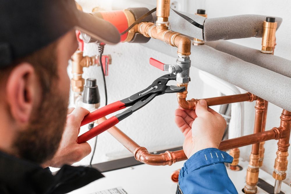 Plumber using pliers to work on copper pipes, indoors.