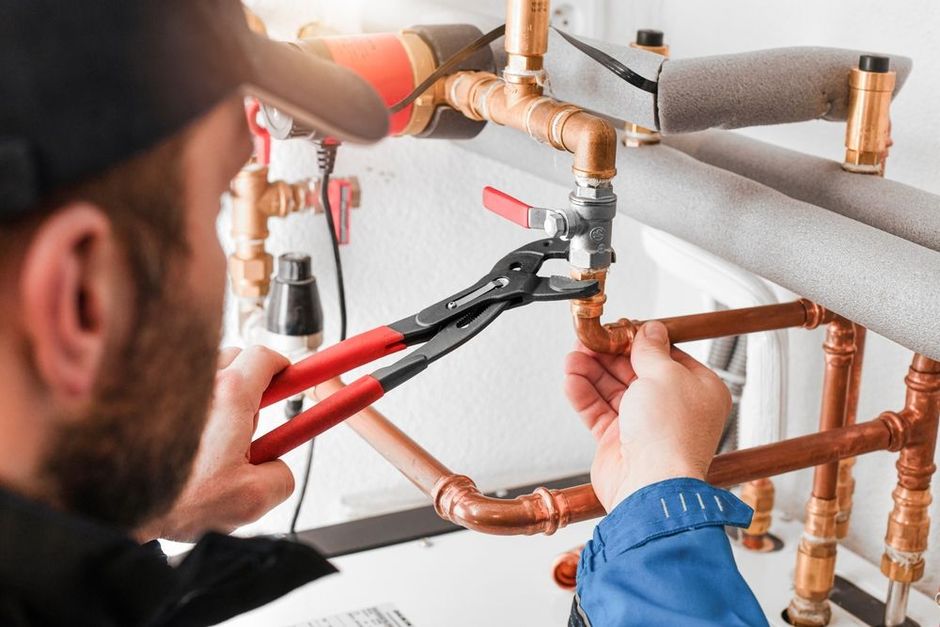 Plumber using pliers to work on copper pipes, indoors.