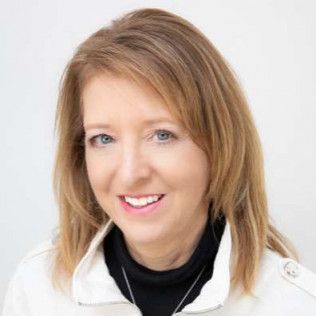 Woman with blonde hair, smiling, wearing a black turtleneck and white jacket.