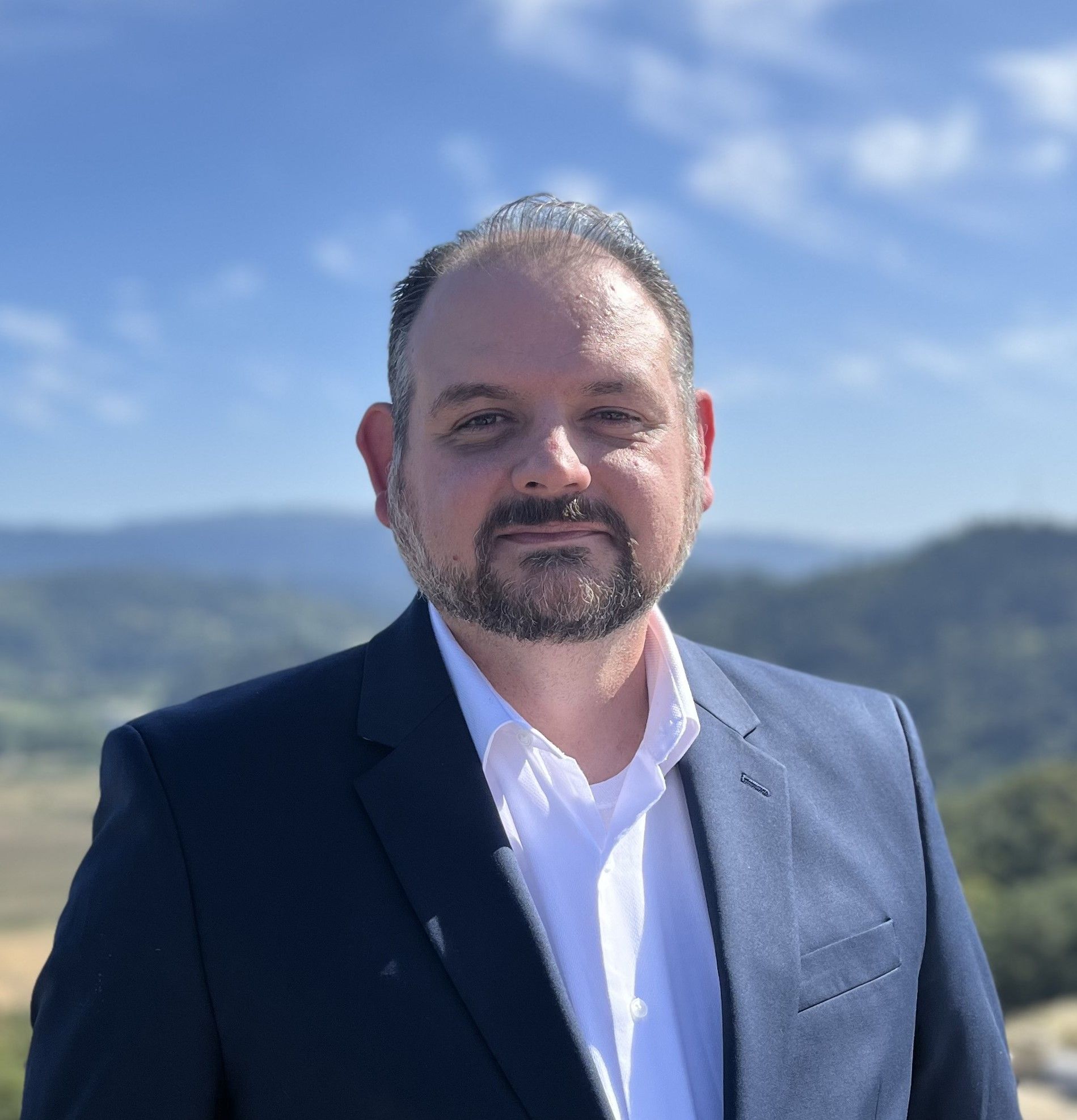 Man in suit with purple striped tie smiles at the camera.