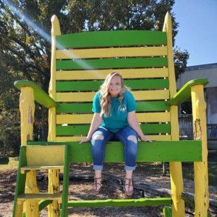 Woman sits on giant green and yellow rocking chair.