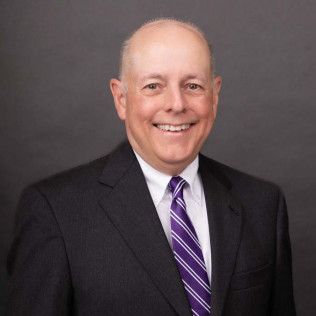 Man in suit with purple striped tie smiles at the camera.