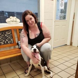 Woman and dog in animal shelter; woman crouches, petting dog. Dog has tongue out.