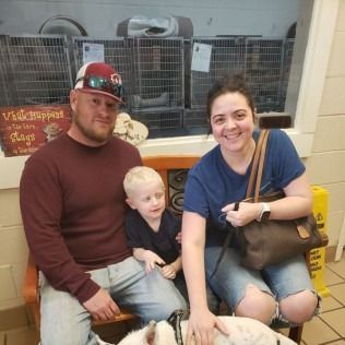 Family sitting on bench at shelter, petting a dog.