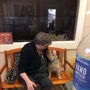 Woman petting a small dog on a bench, next to a hand sanitizer bottle.
