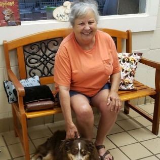 Woman petting a dog sitting on a wooden bench indoors, smiling.