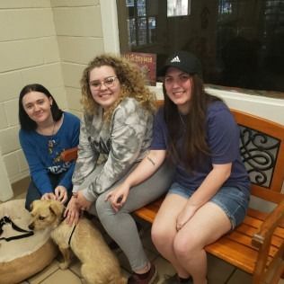 Three people petting a dog on a bench at an animal shelter.