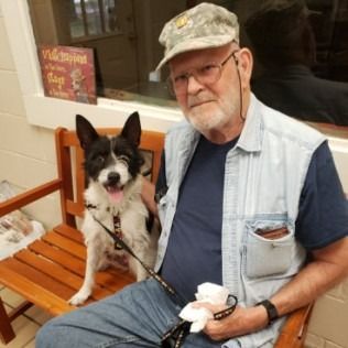 Man sitting on a bench with a black and white dog at a facility. The dog is on a leash.