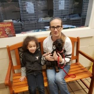 Woman and child on a bench, holding a puppy in a shelter.