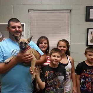 Family with puppy in a room with blinds, smiles, and holding dog.