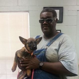 Man in overalls holding a puppy, both looking at the camera.
