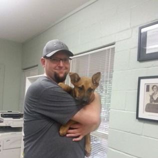Man in cap holding brown puppy by a window.