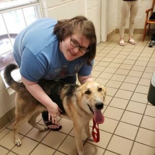 Woman petting a tan and black dog indoors. Both are smiling. Tile floor.