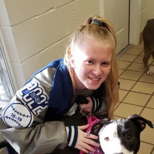 Person in jacket smiles, holds dog on leash indoors. Dog is black and white.