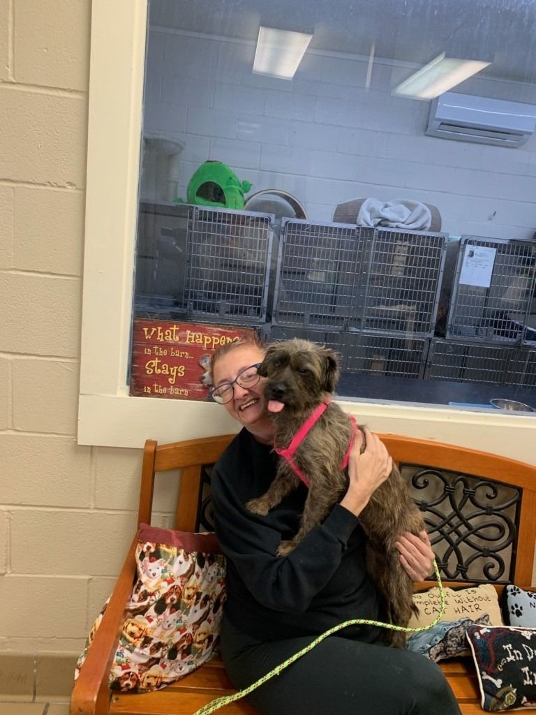 Woman hugging a small dog in a shelter. The dog has its tongue out, smiling.