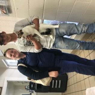 Person holding a cat, standing near a person in blue. Both are in a building.