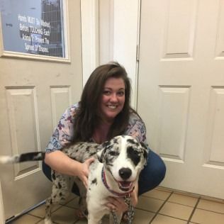 Woman smiles, crouched next to a spotted dog indoors. White and beige doors and tile.
