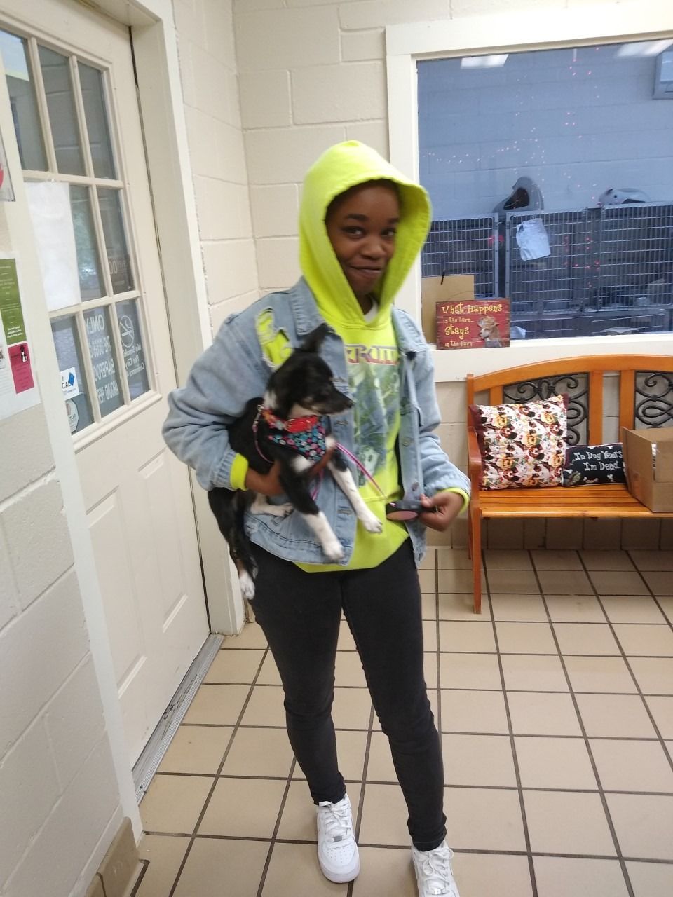 Person in neon hoodie holds small black and white dog indoors, smiling.
