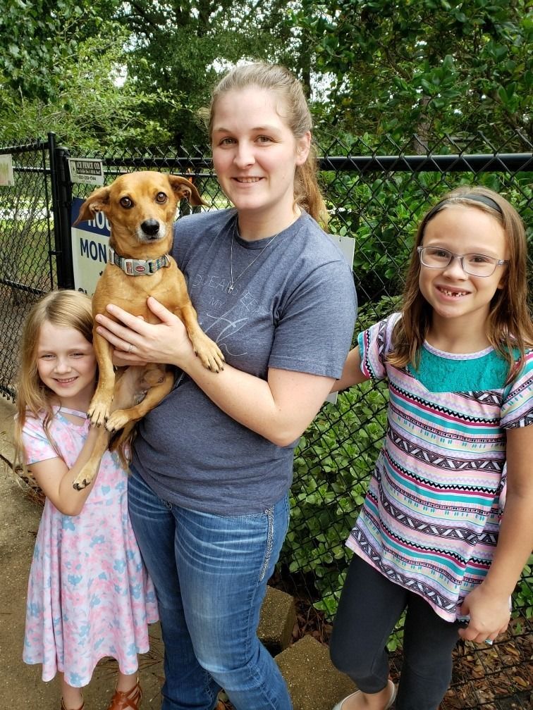 Woman and two girls with a dog in a fenced area; they are smiling.