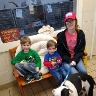 Woman and two children sit on a bench with a black and white dog at a shelter.