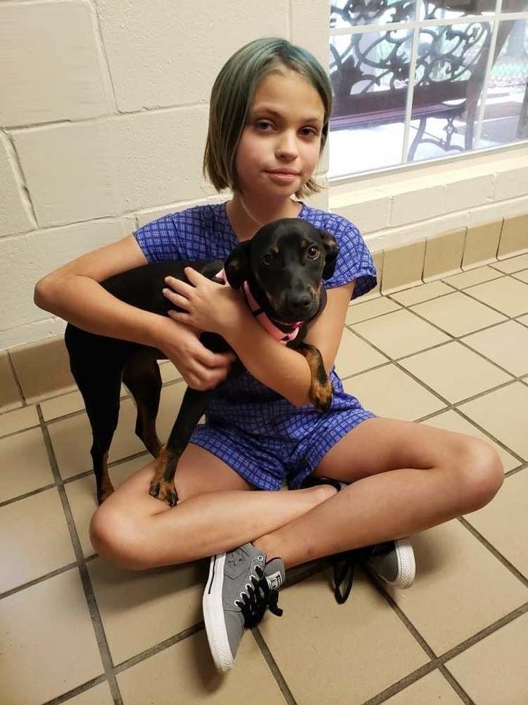 Girl sitting cross-legged, holding a black and tan puppy. They are indoors.