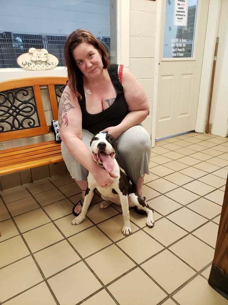 Woman kneeling, petting a black and white dog in a tiled room near a wooden bench.