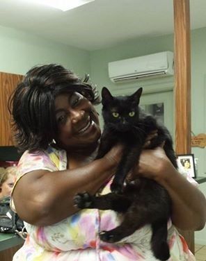 Woman smiling, holding a black cat indoors, possibly a clinic.