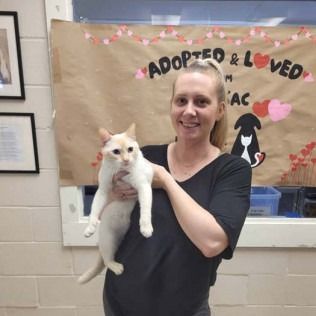 Woman holding a light-colored cat in front of a banner that says