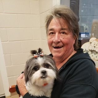 Person smiling, holding a Shih Tzu dog with a bow in its hair.