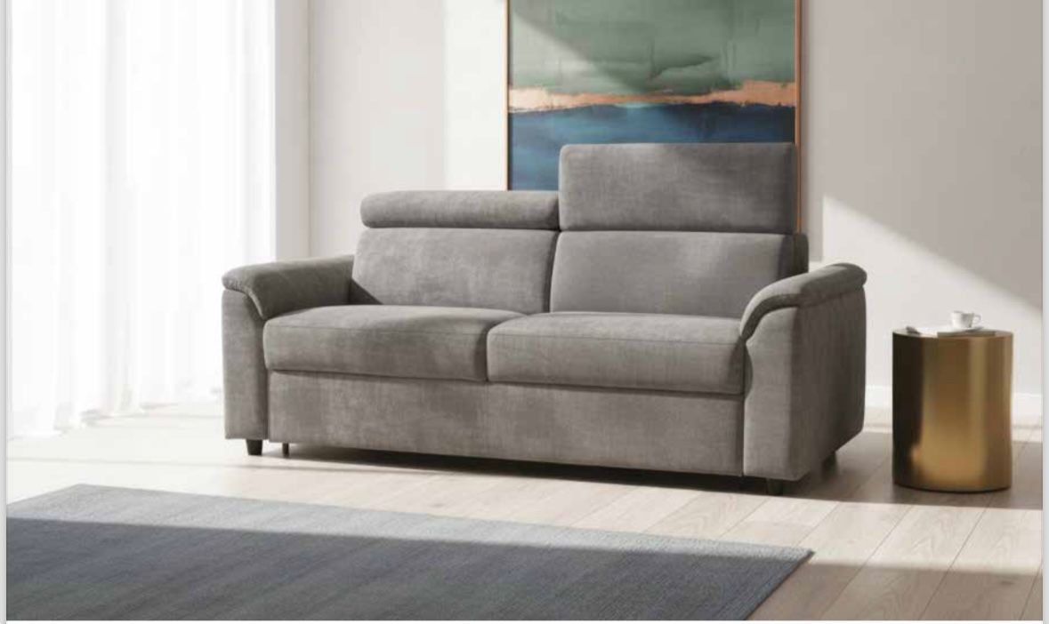 Un divano grigio con poggiatesta regolabile in una stanza luminosa e moderna, accanto a un piccolo tavolino dorato.