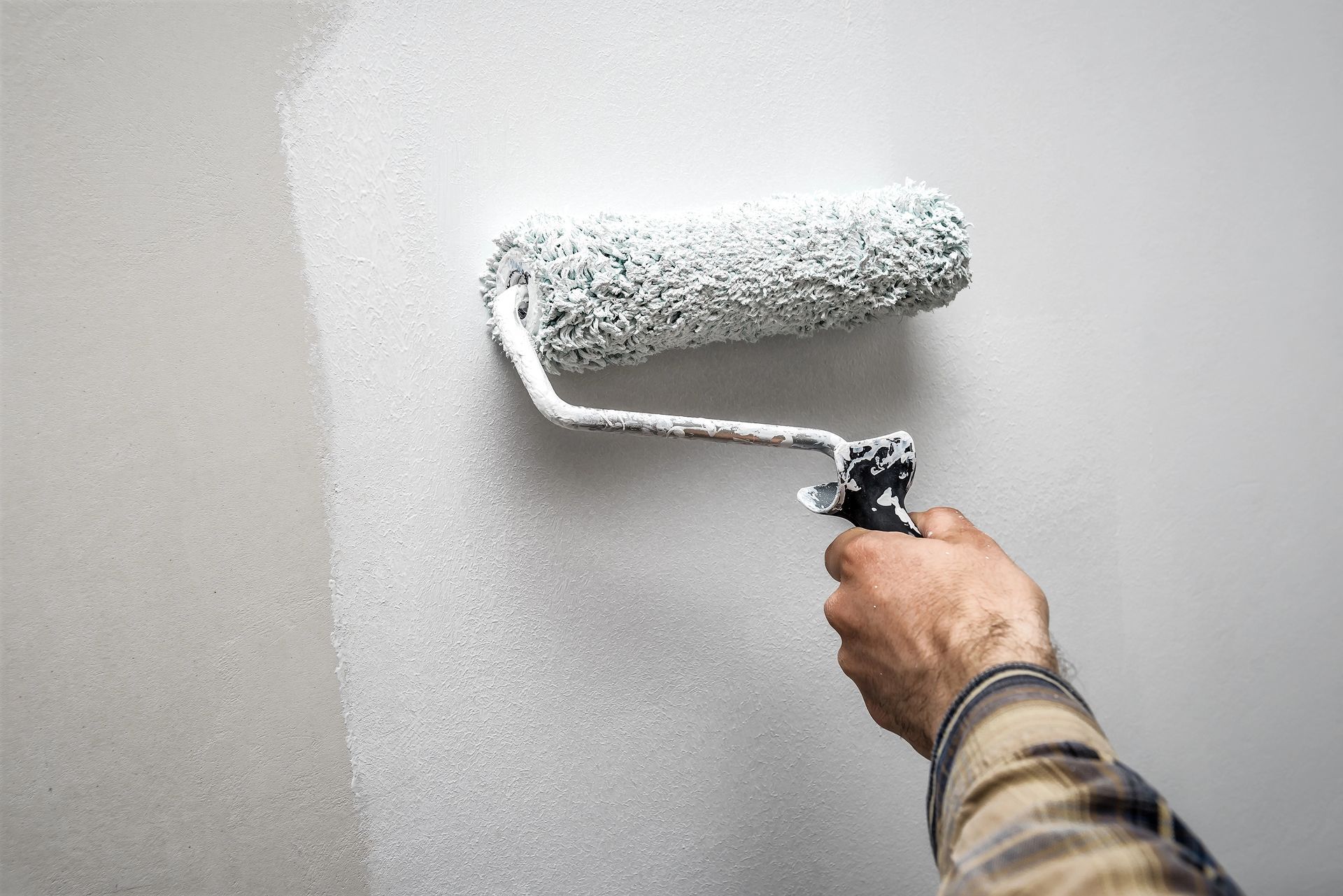 A person is painting a wall with a paint roller.