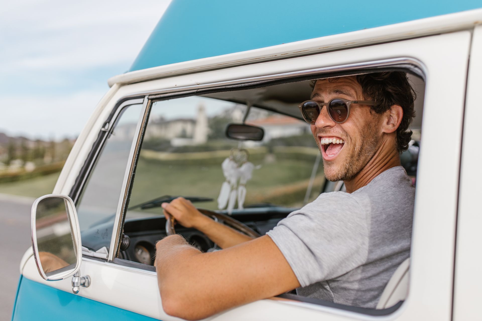 Man driving a blue and white van, smiling, wearing sunglasses.