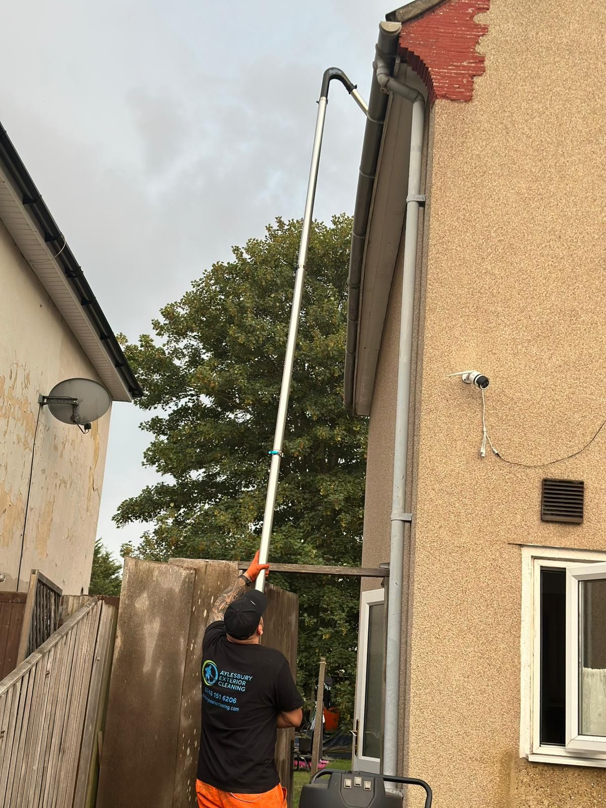 A man in a yellow vest is cleaning a gutter on the side of a house.