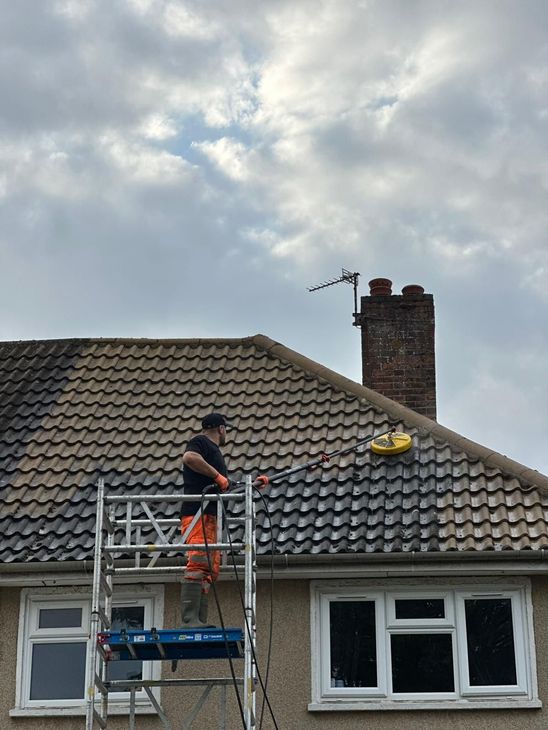 A person is cleaning the roof of a house with a high pressure washer.