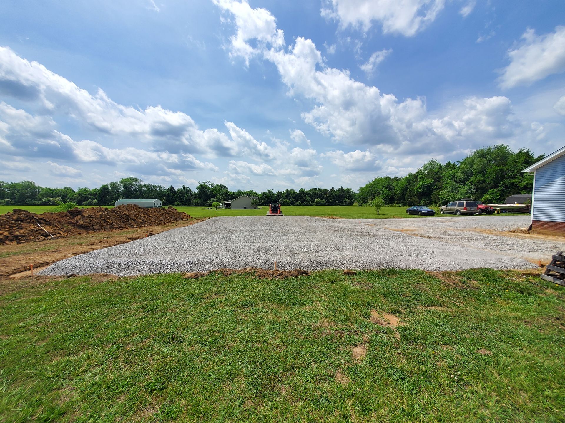 A gravel driveway is being built in a grassy field next to a house.