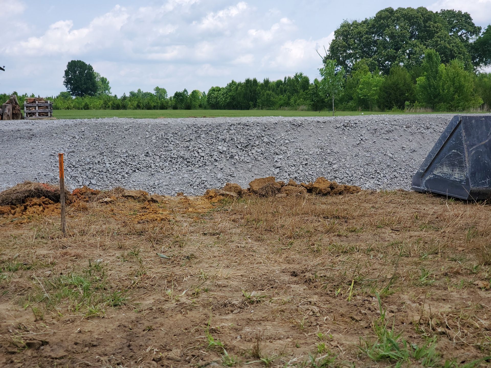 A large black bucket is sitting in the middle of a dirt field.