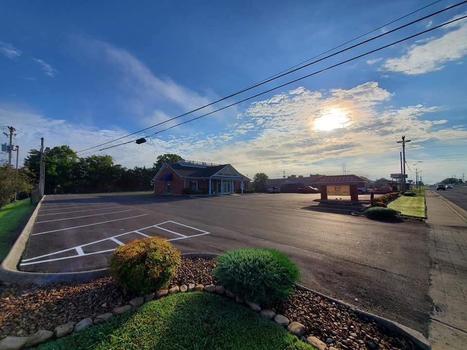 A parking lot with a building in the background and the sun shining through the clouds.